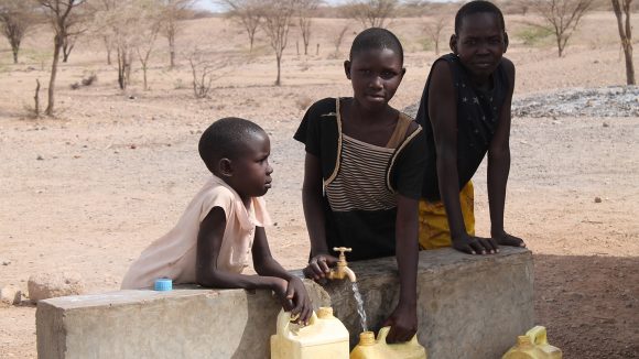 Three children lean over a wall and fill yellow containers with water from a tap.