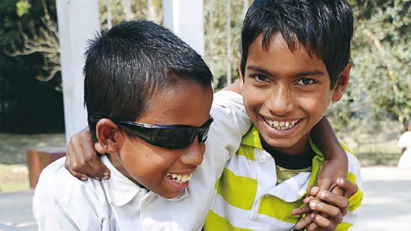 From the cover of Sightsavers annual report 2009: two boys smile with their arms round each other.