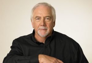 Portrait of Brien in black shirt against white background.