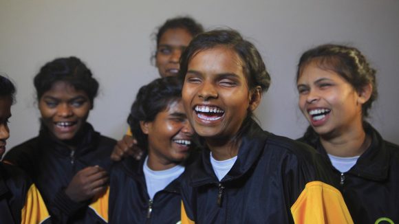 A group of visually impaired girls wearing Sightsavers tracksuits, laughing.