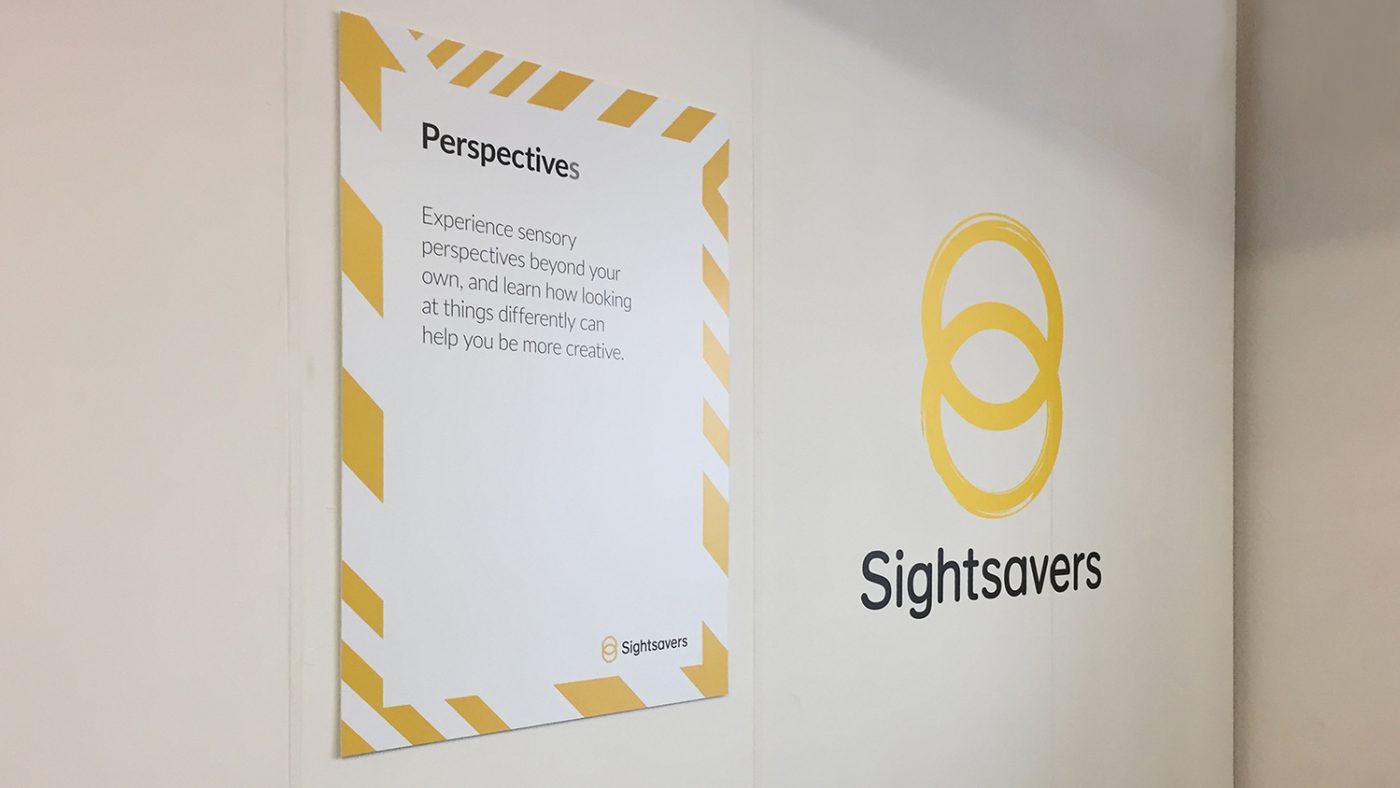 The front of Sightsavers' stand, featuring a logo and a sign with the word 'Perspectives'.