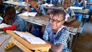 Student Ariane smiles at her desk while wearing her new glasses.