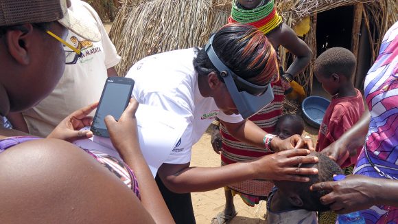 Eye health staff examine a child's eyes and record the results on a mobile phone.