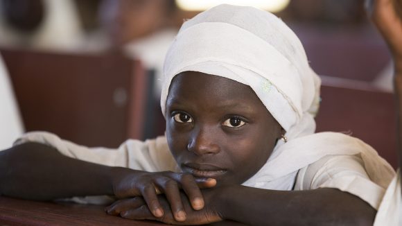 Seven-year-old Dorcas from Nigeria sits with her chin on her hands and looks at the camera.