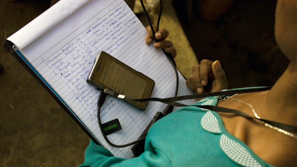 An eye care worker holding a notepad with a phone resting on top.