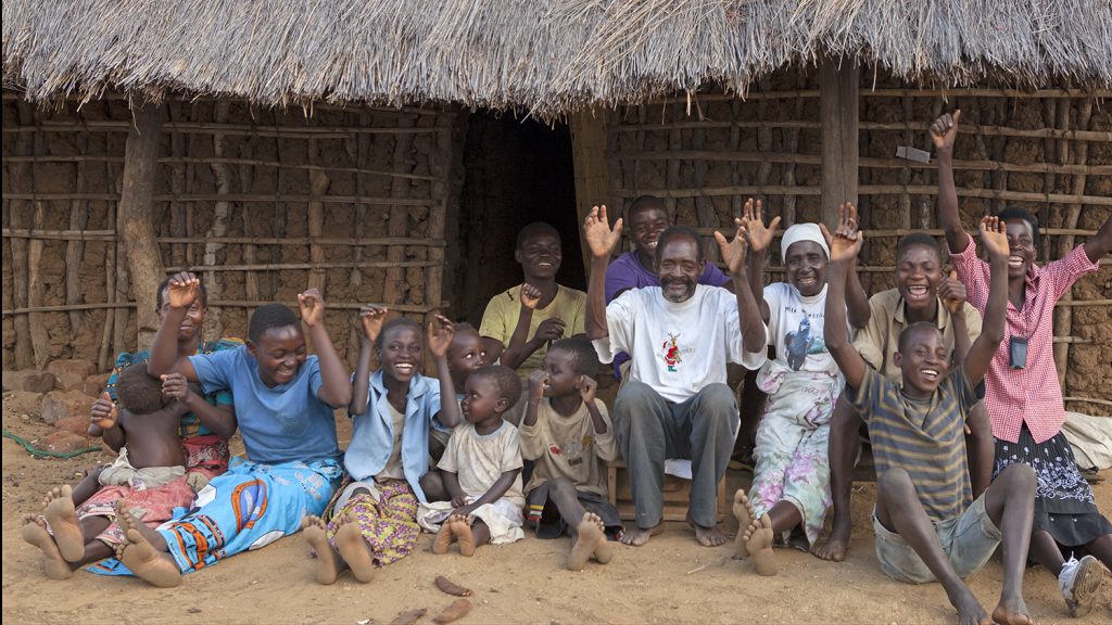 Winesi smiles with his family outside their home in Malawi.