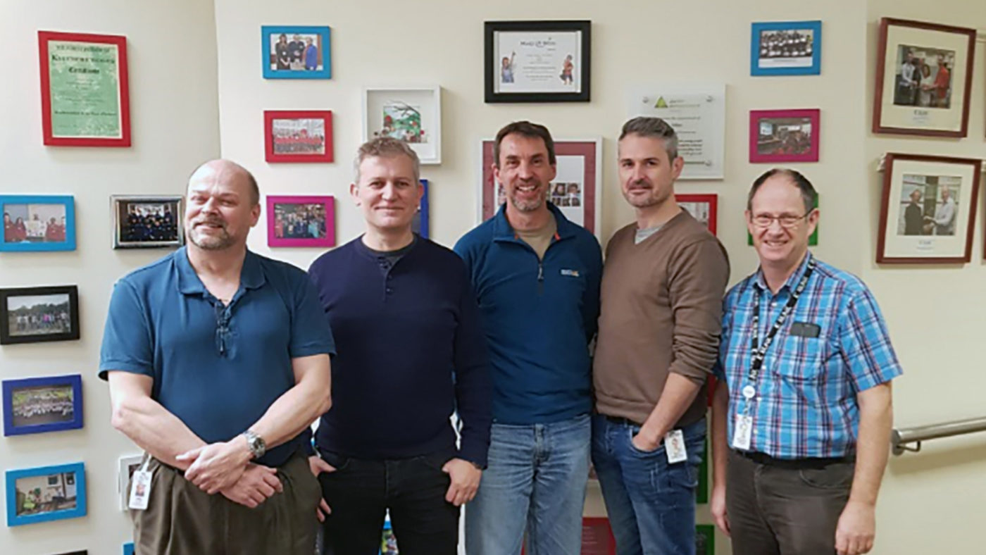 A group of staff from Xilinx atand in front of photos and pictures from the exhibition.