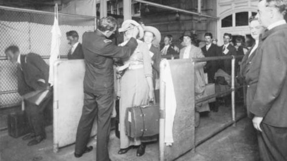 An old black and white photo of a woman getting her eyes screened for trachoma at an immigration check point at Ellis Island, USA.