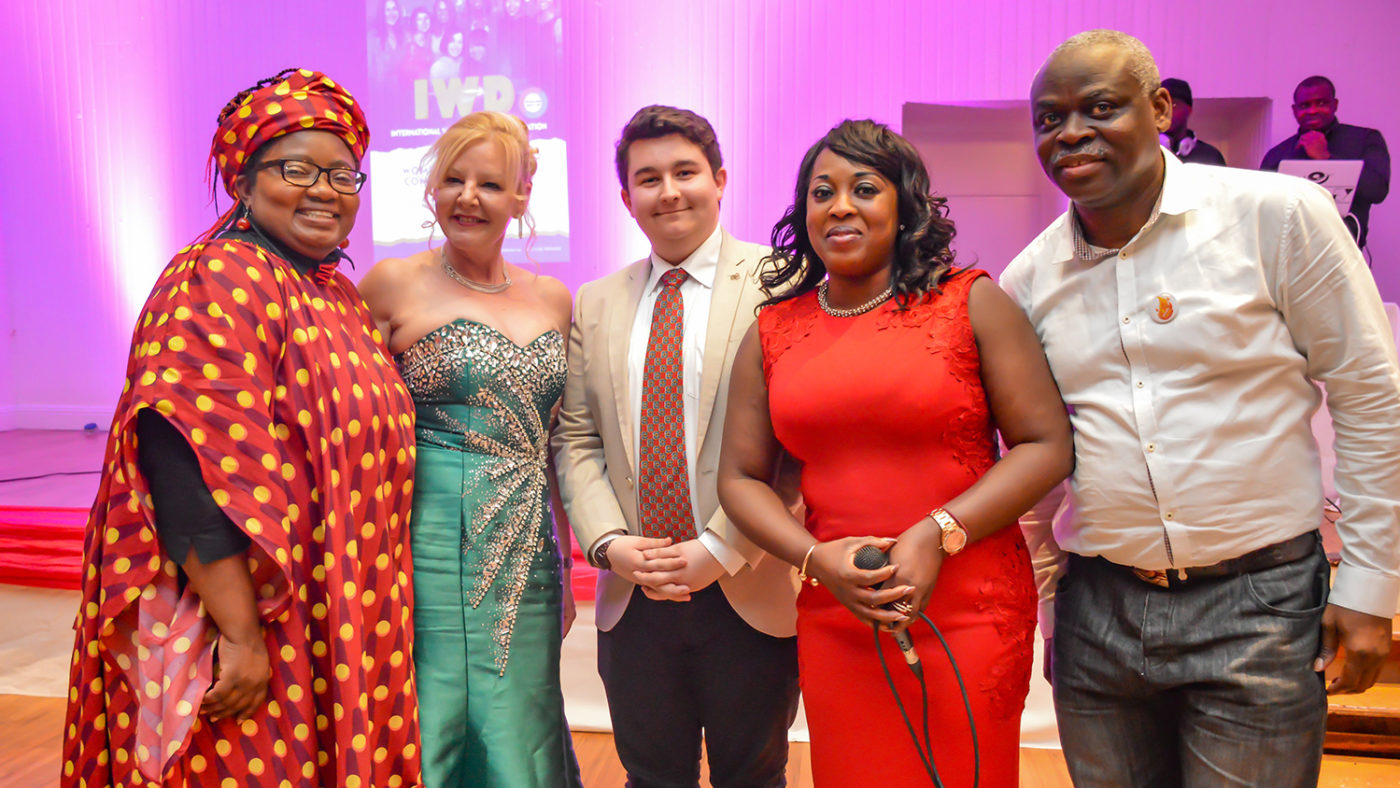 A group of guests in colourful formal clothes smile at the camera.