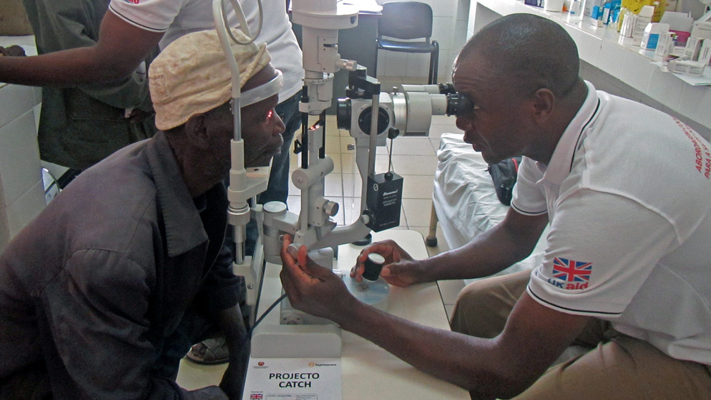 A patient has his eyes checked by a health worker.