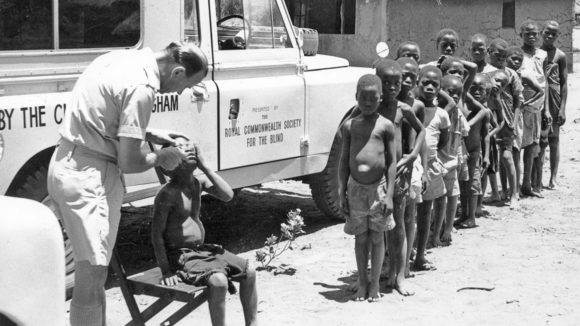 A black-and-white image from Malawi in 1965, showing children lining up to have their eyes examined.
