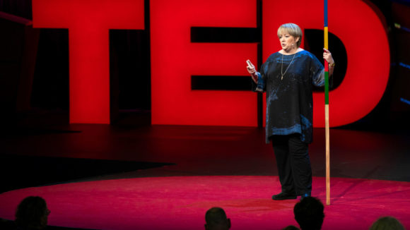 Sightsavers CEO CAroline Harper during her TED Talk, standing in front of large red letters spelling TED.