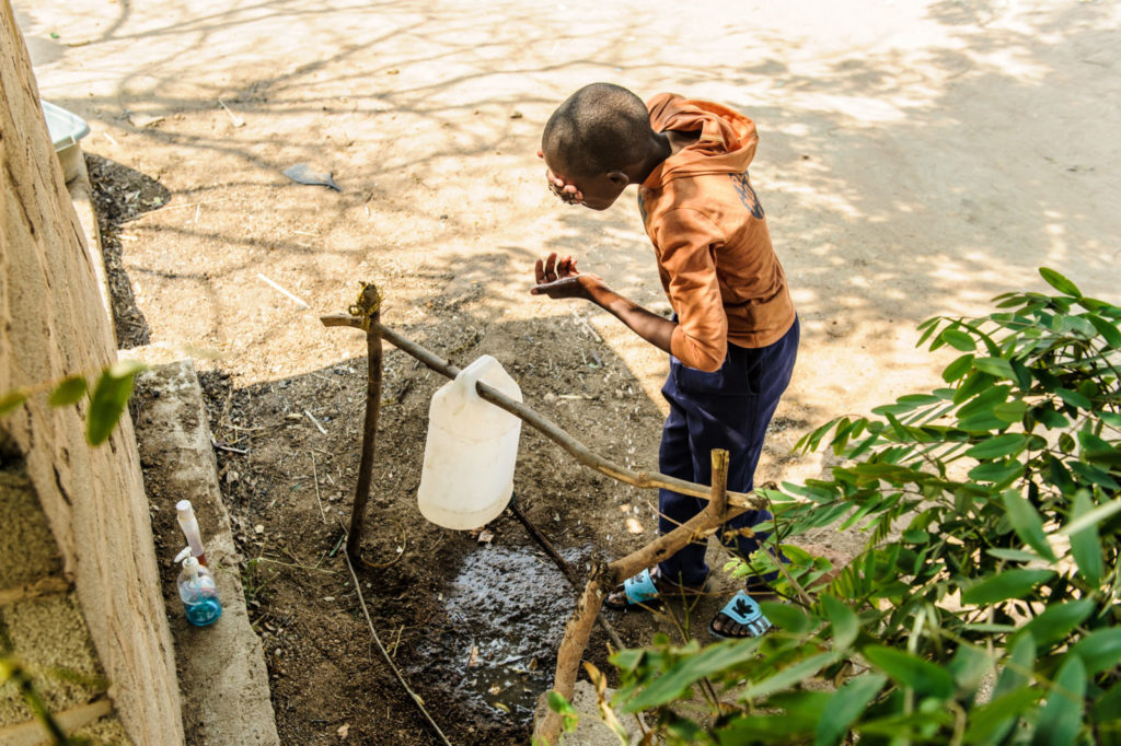 A boy washes his face using a tippy tap, a hygienic handwashing device in areas where clean water is scarce.