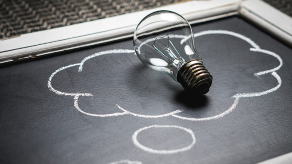 A thought bubble drawn on a chalk board, with a lightbulb positioned inside it.