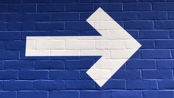 A white arrow symbol painted on a blue wall, pointing to the right.