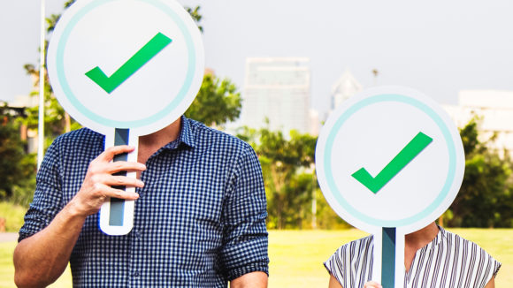 Two people holding up signs with tick marks on them.