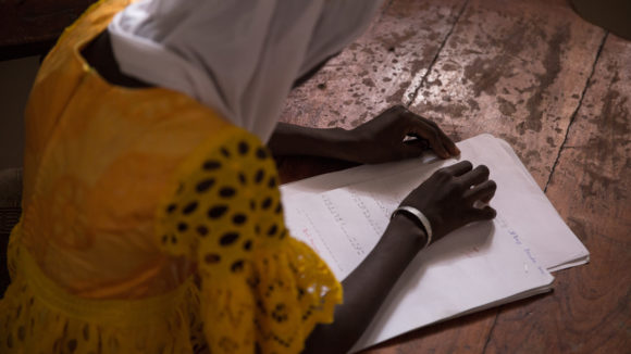 View over the shoulder of a young woman who is reading a braille document with her hands.