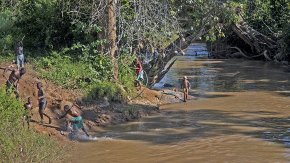 Children playing in the water, a man collecting sand to sell it.