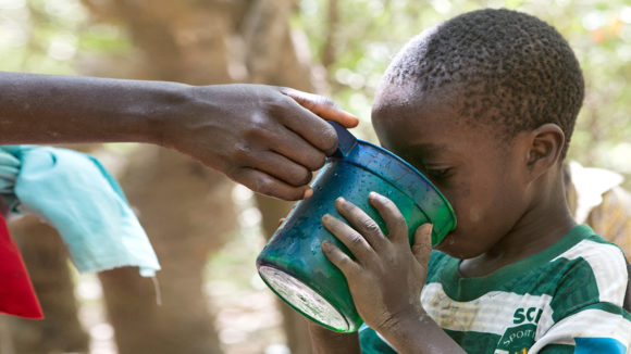 A child drinks water from a cup during a drug administration session in Nigeria.