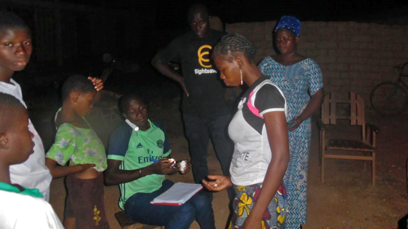 A volunteer in Burkina Faso gives out medication in the dark.