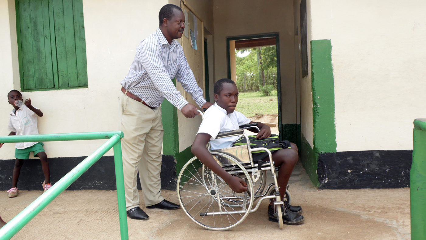 A student in a wheelchair is pushed by a teacher at a school in Kenya.