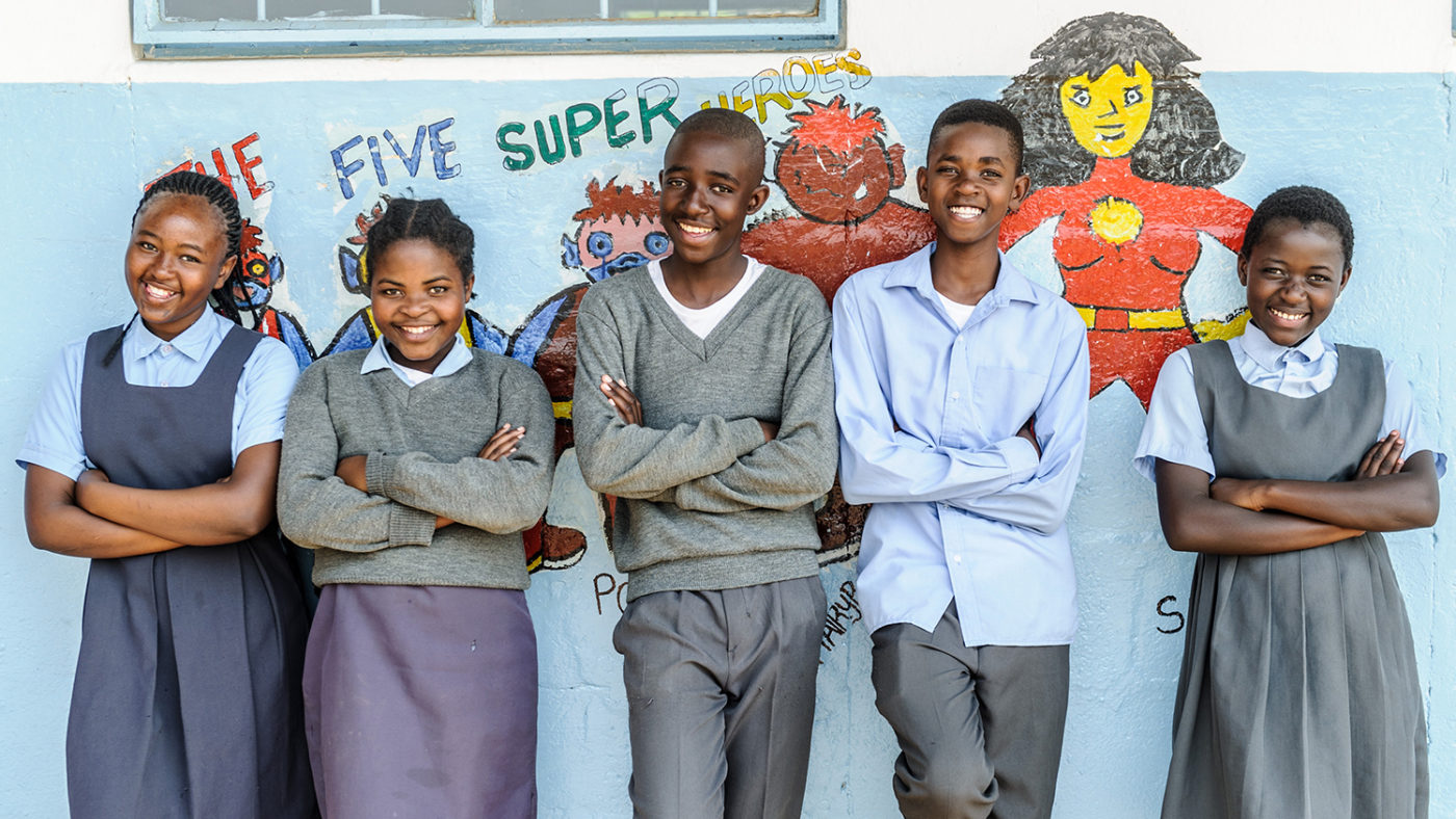Five school students in Zambia in front of a mural depicting superheroes from Sightsavers' Super School of 5 programme.