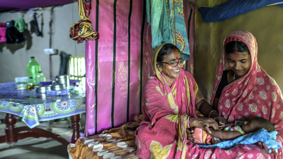 A lady with glasses looks at her grandchild and smiles.