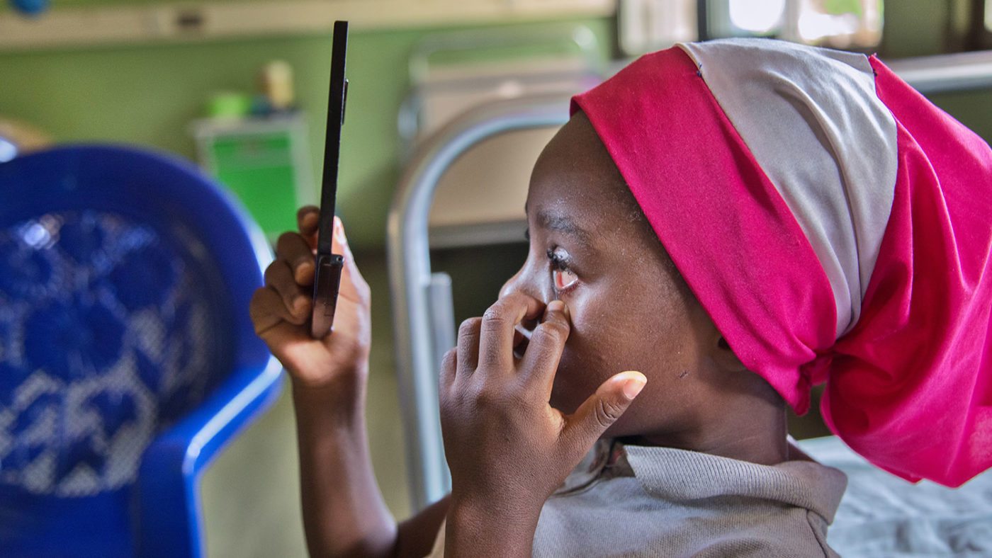 Khadijah checks her eye in the mirror after her surgery.