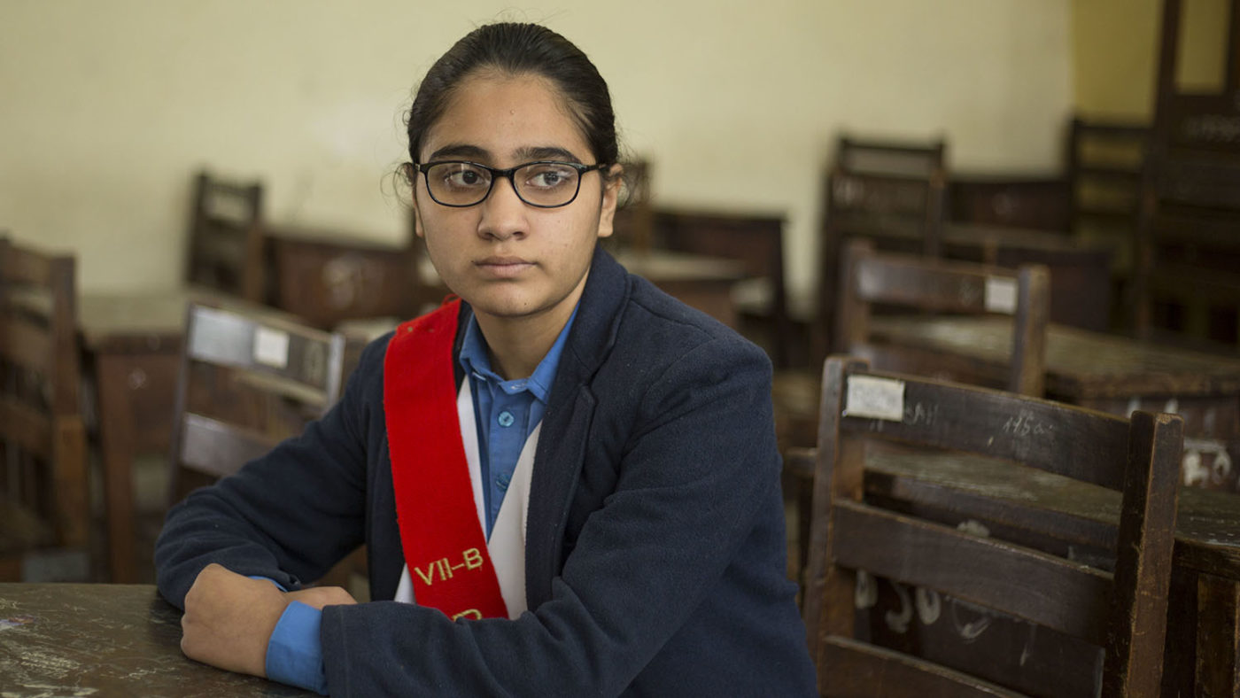 A girl with glasses sits in the classroom.
