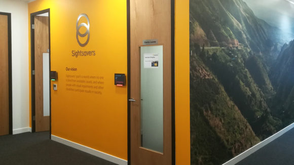 A Sightsavers office wall in yellow, featuring the logo and a large photo on the adjacent wall.