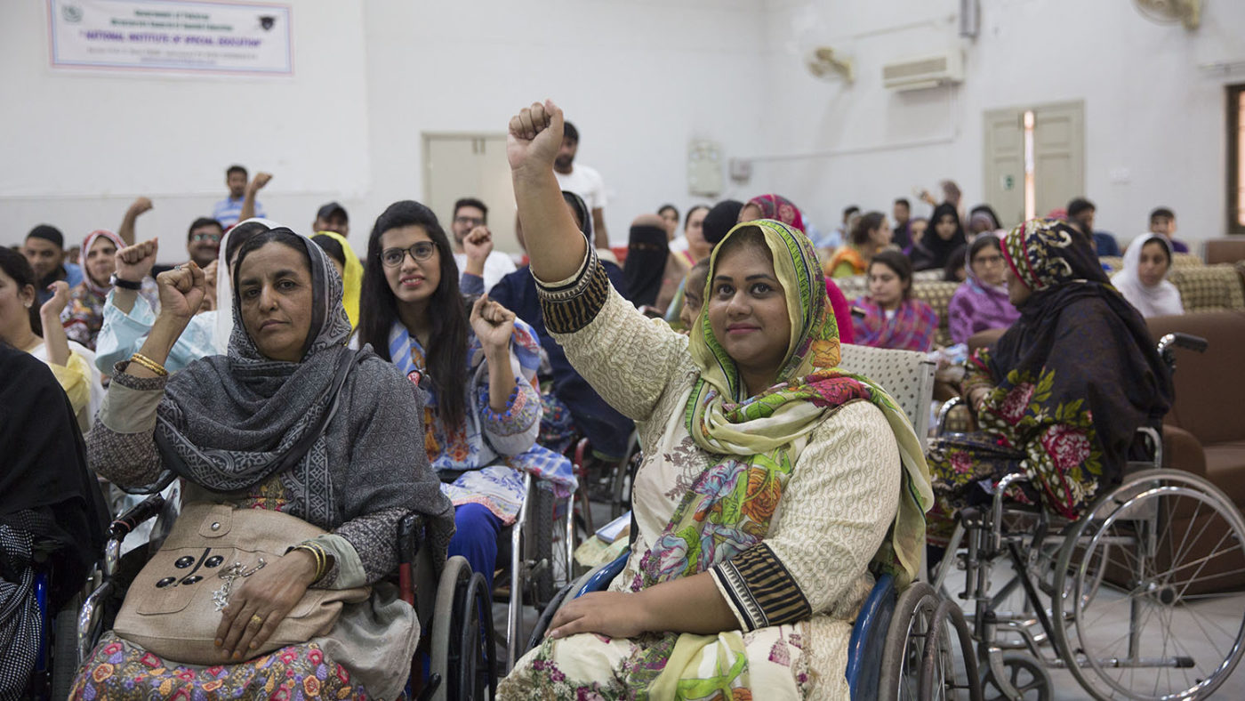 A group of people with disabilities raise their hands.