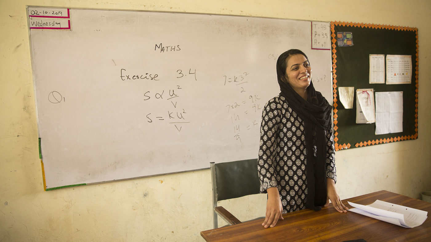 A teacher stands in front of a white board.