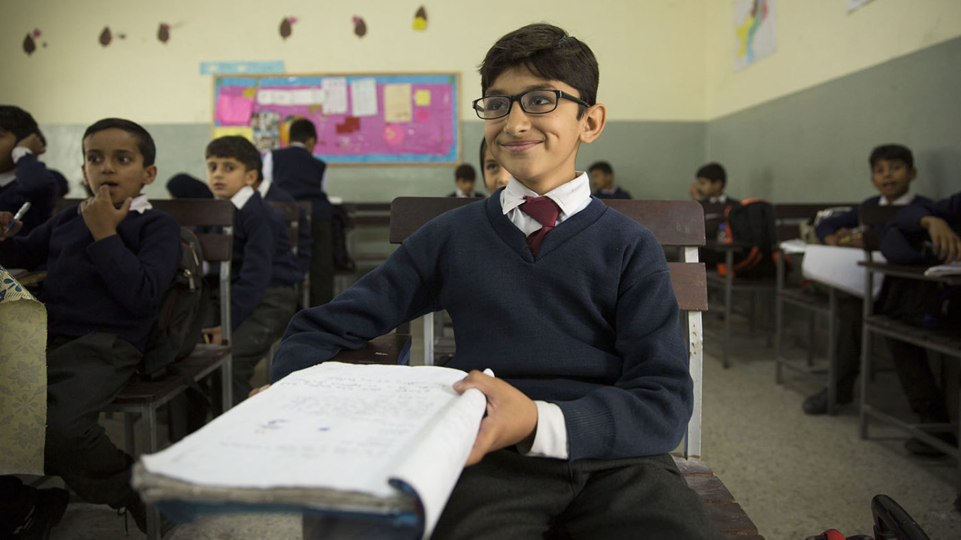 A boy wearing glasses smiling in the classroom.
