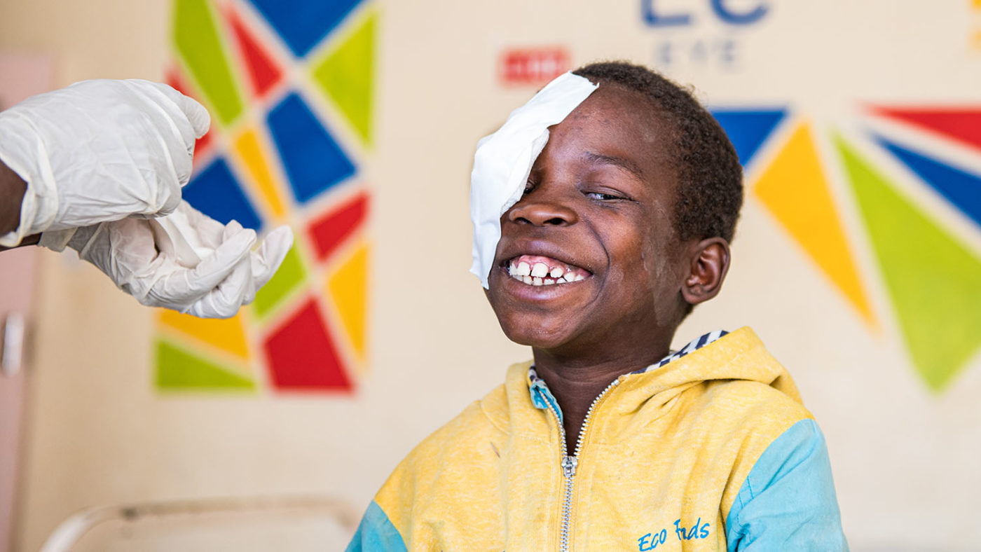 Boy smiling from ear to ear after having a bandage removed from his eye.