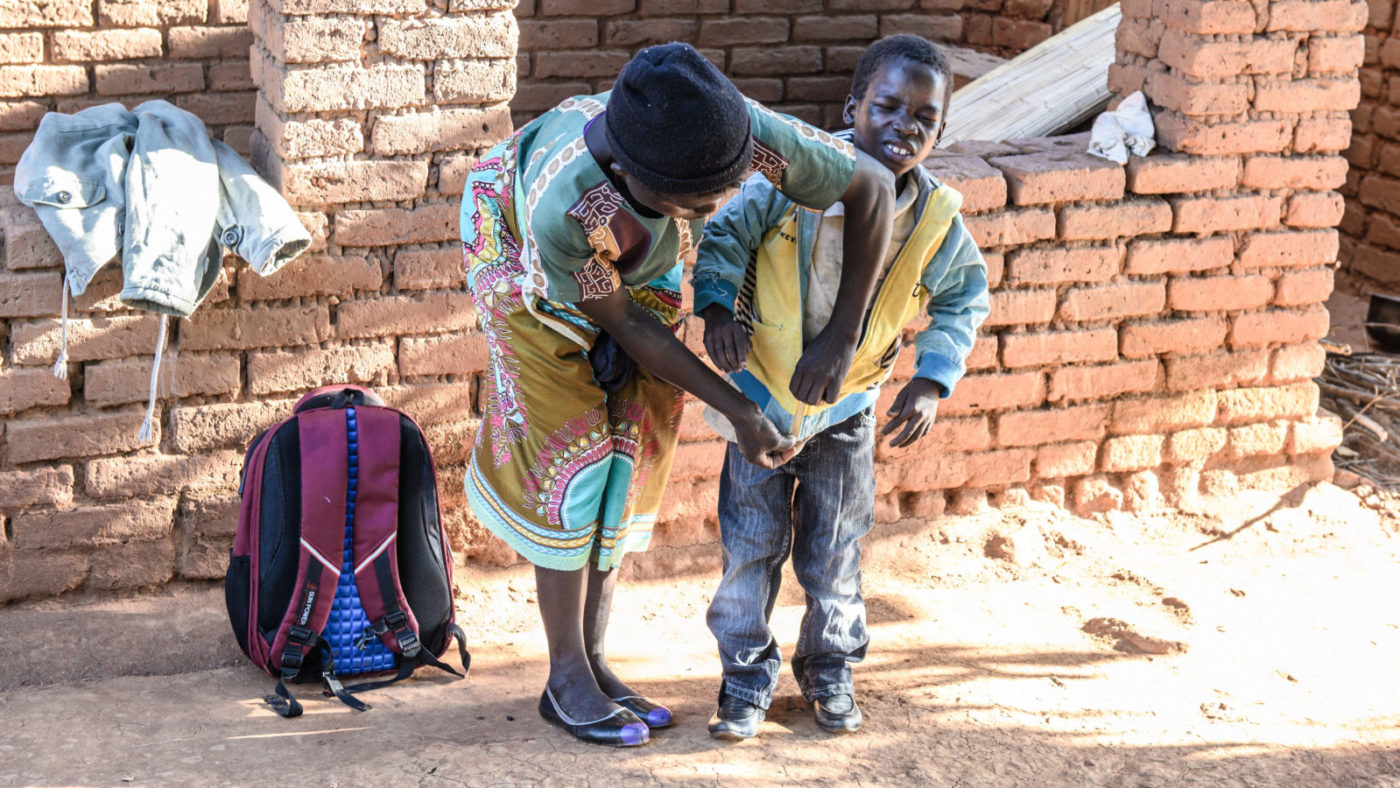 Zelina zips up her son's coat. Taonga is looking uncomfortable with his eyes.
