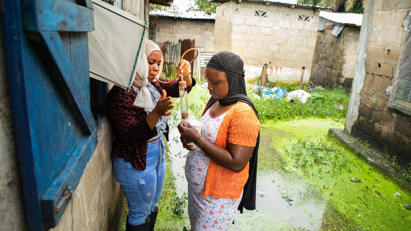 Two women are shown collecting mosquitoes using a trap.