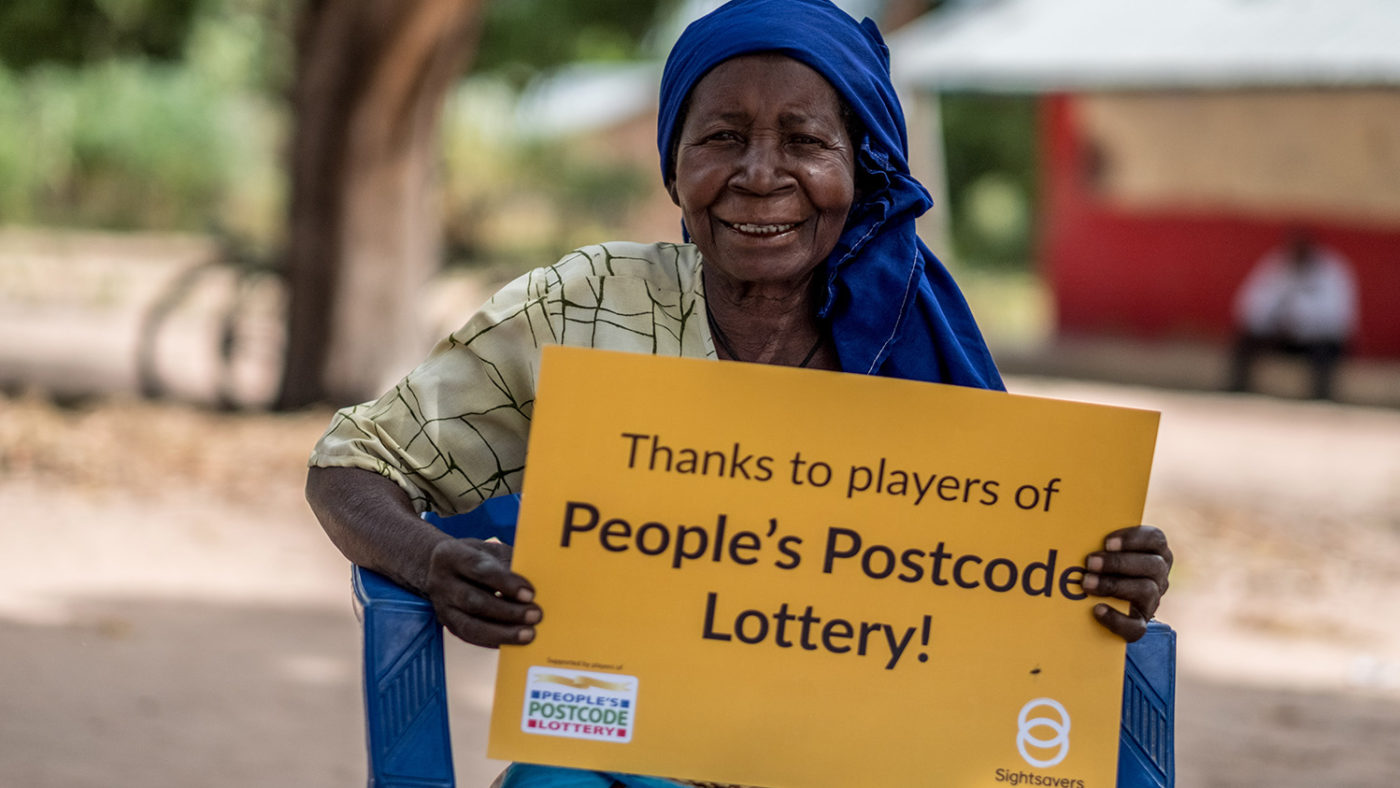 Aziza holds a sign saying 'Thanks to Players of People's Postcode Lottery'.