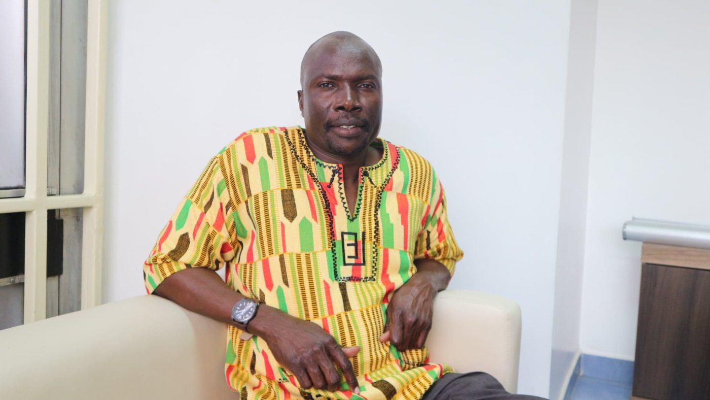 Shikuku Obosi sits, smiling at the camera.