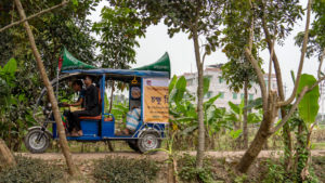 A tuk tuk passes through a village.