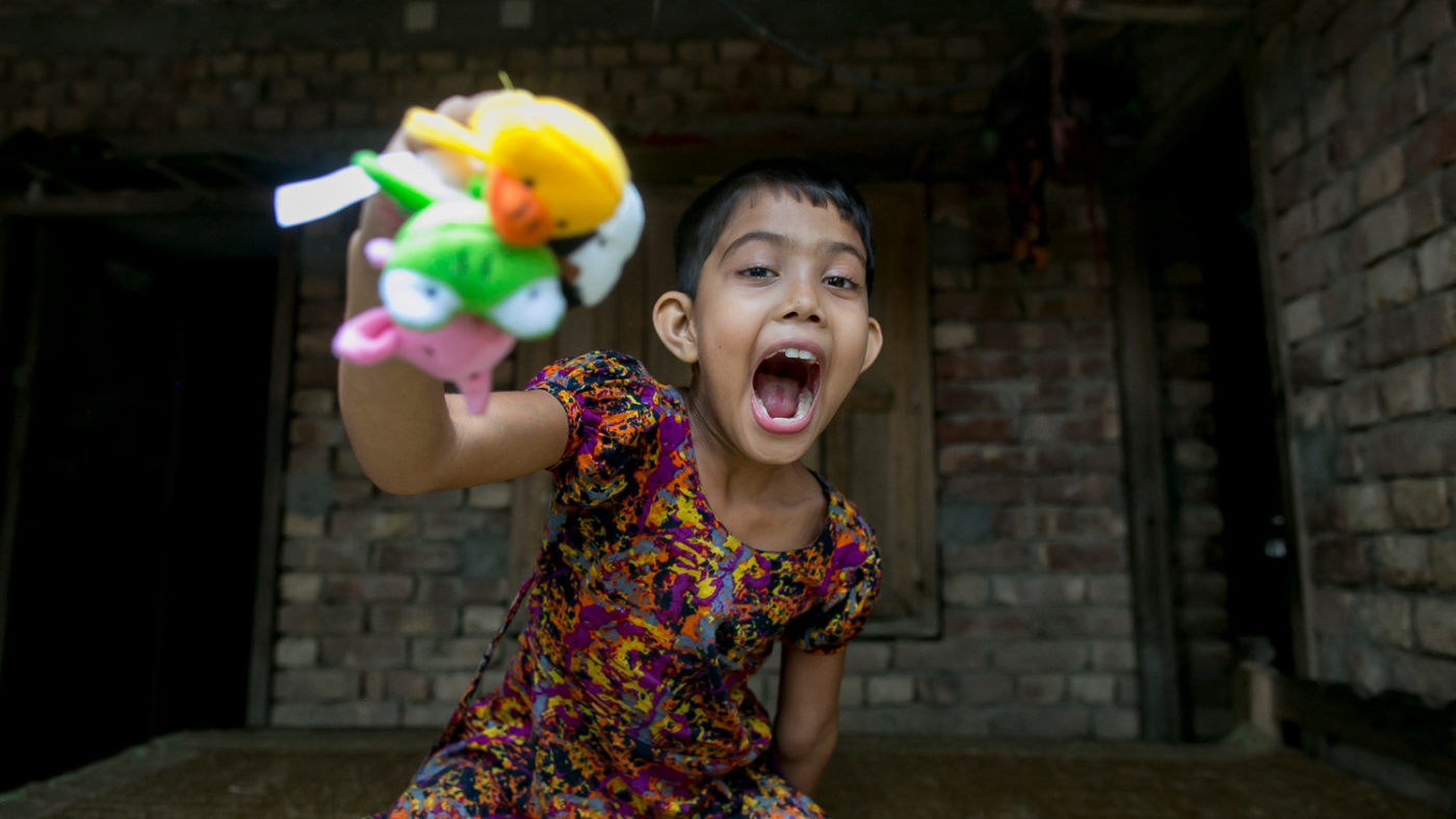 Muslima smiling gleefully with her mouth open, while playing with three colourful finger puppets.