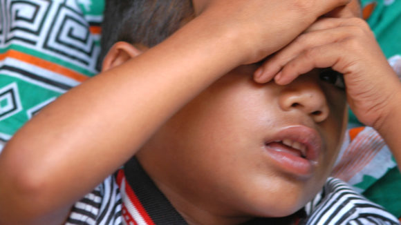 A young boy covering his eyes with his hands.