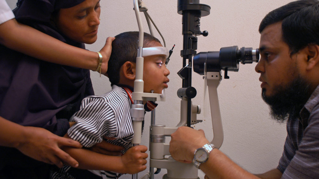 A young boy having his eyes checked by a health worker.