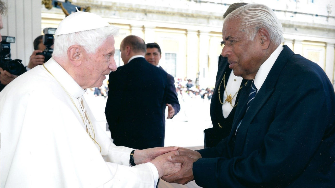 The Pope holds hands and greets another man.