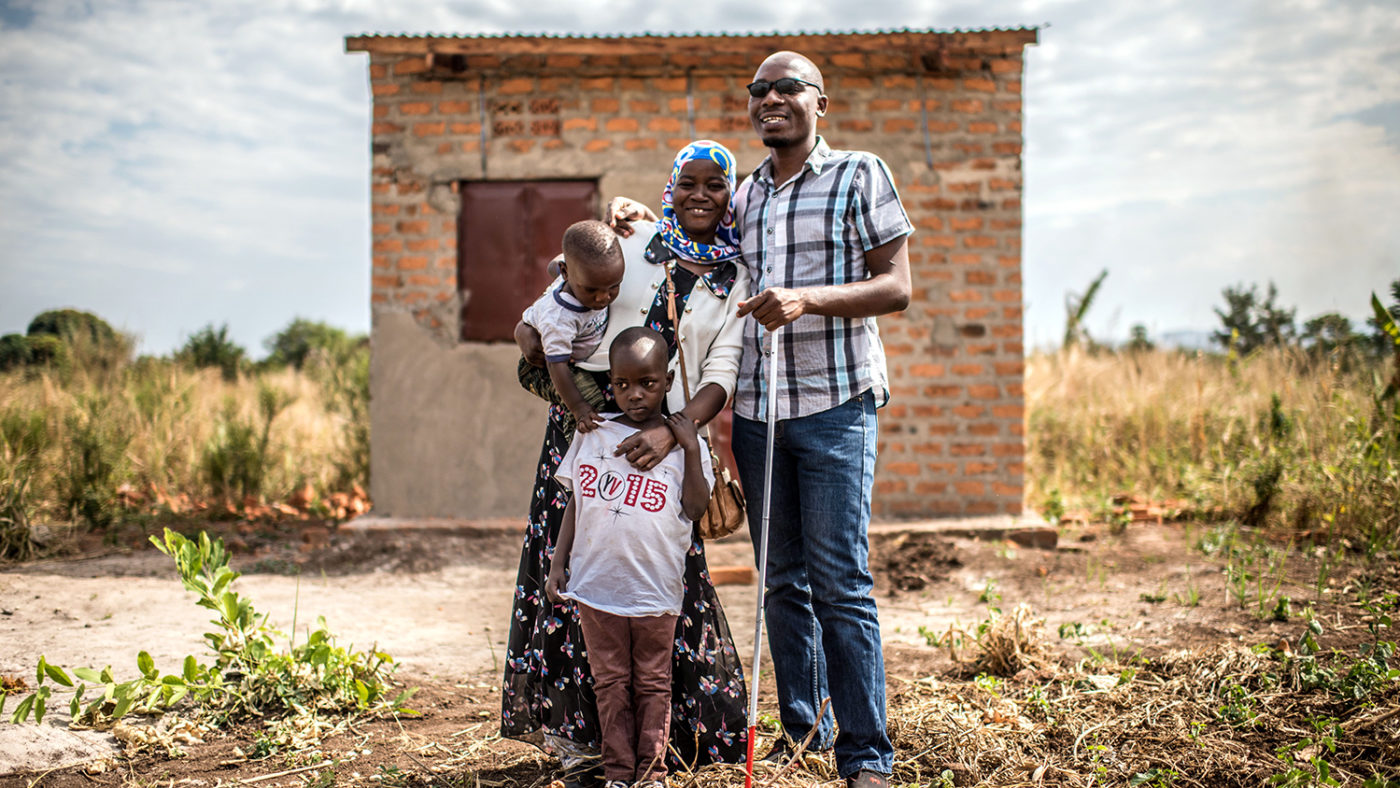 Husband and wife, with two children, stand outside their home.