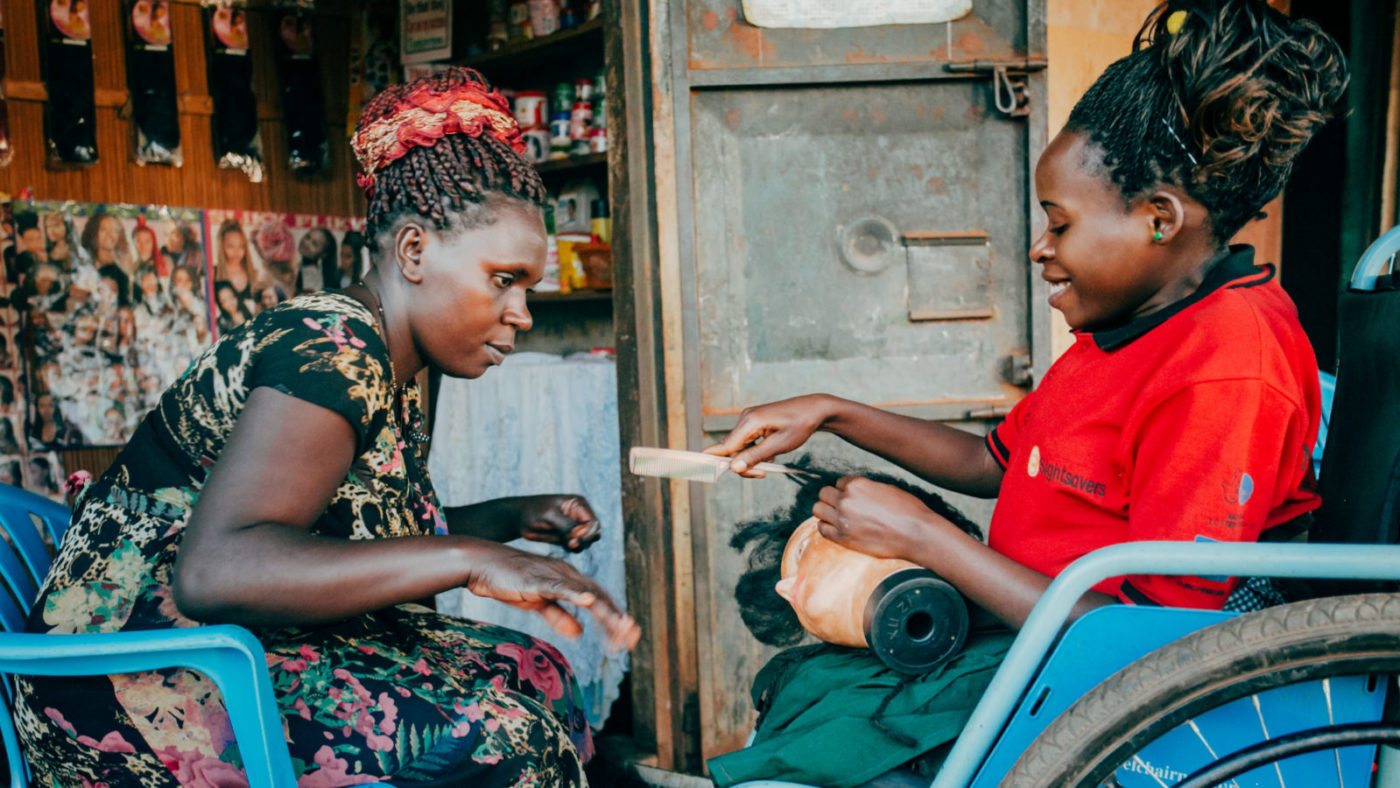 A young woman using a wheelchair sits outside a hairdressing salon with her employer.