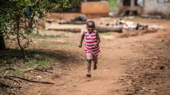 Asha runs down the road towards the camera