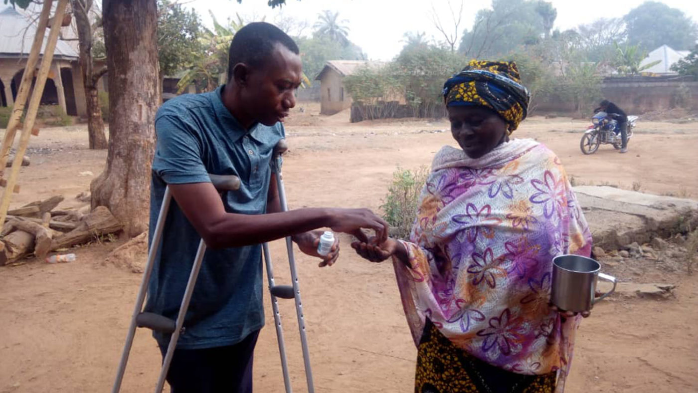 A community volunteer with a disability gives a woman treatment for NTDs.