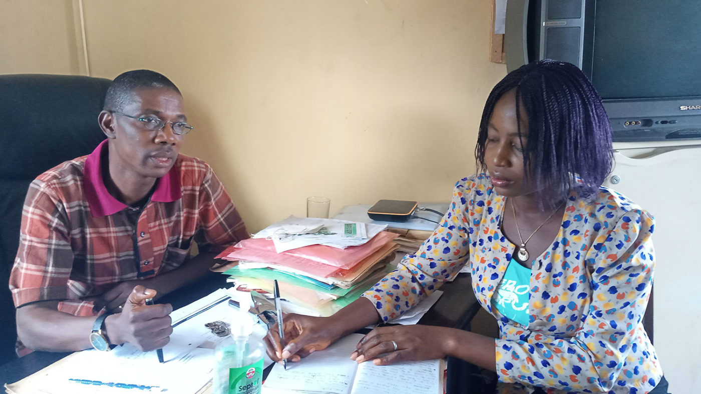A man speaks with a woman at a desk in the office.
