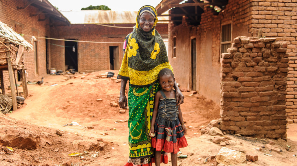 Fatuma and her granddaughter Philly smiling as they stand outside their red clay-brick house