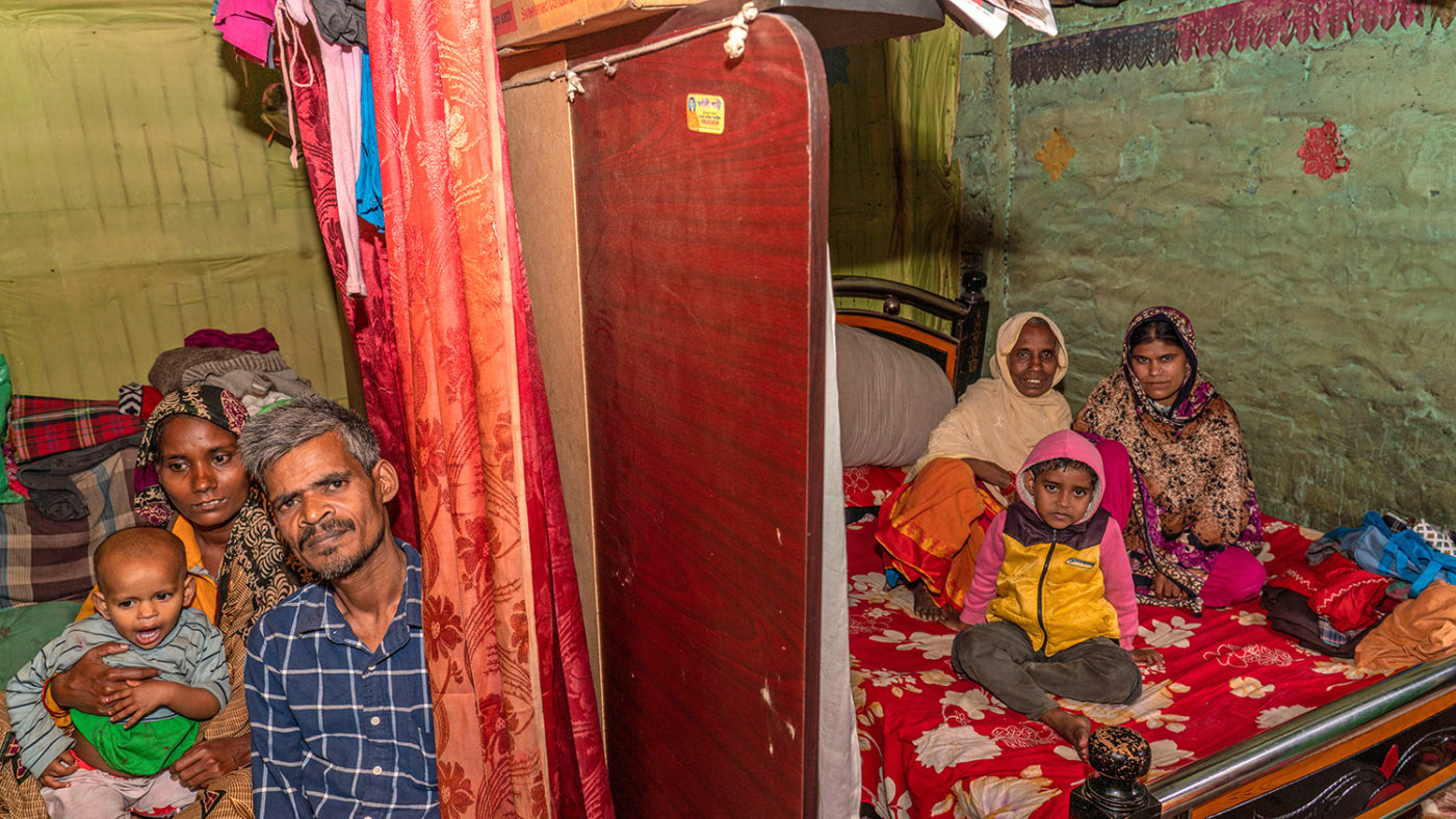 A family sit on beds inside a small room.